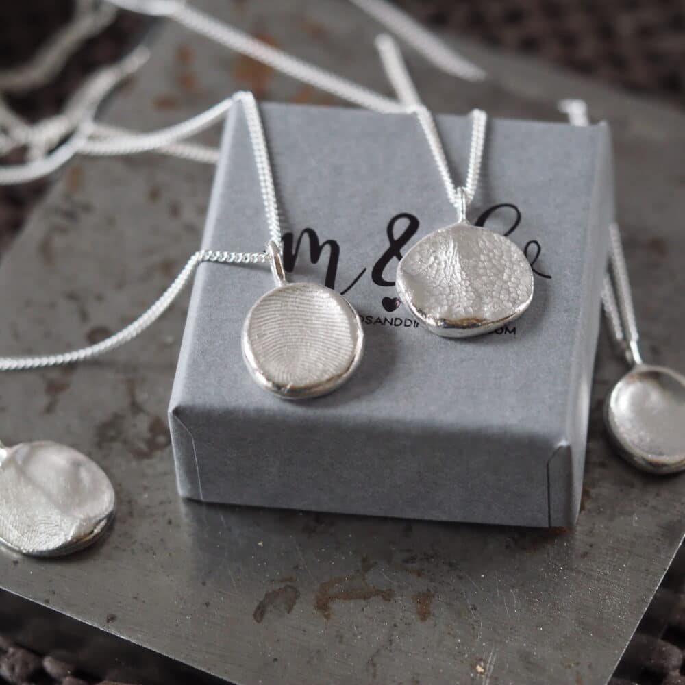 silver fingerprint and dog nose print impression necklaces placed on a gift box
