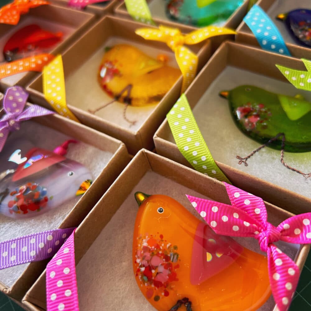 A close up photo of gift boxes containing colourful little handmade quirky birds.