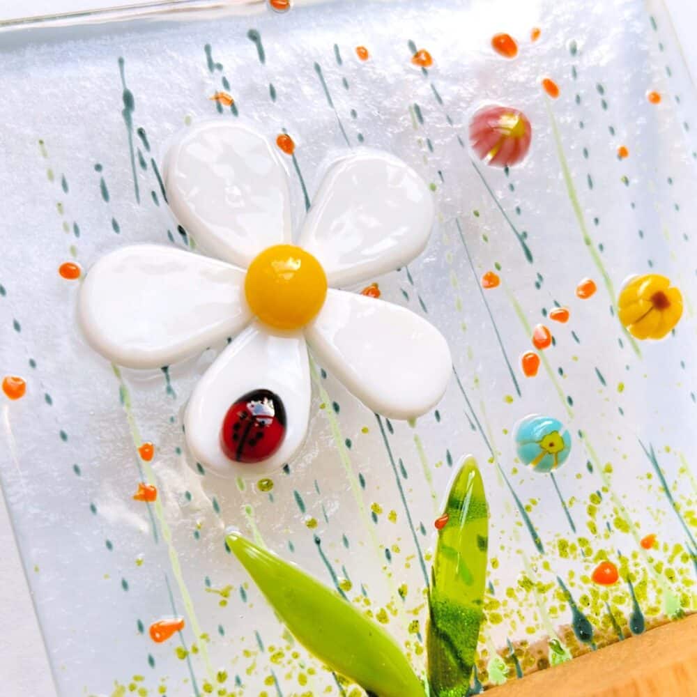 A close up photo of the detail in one of Sarah's floral panels. It shows a white daisy surrounded by grass, little flowers and a ladybird.