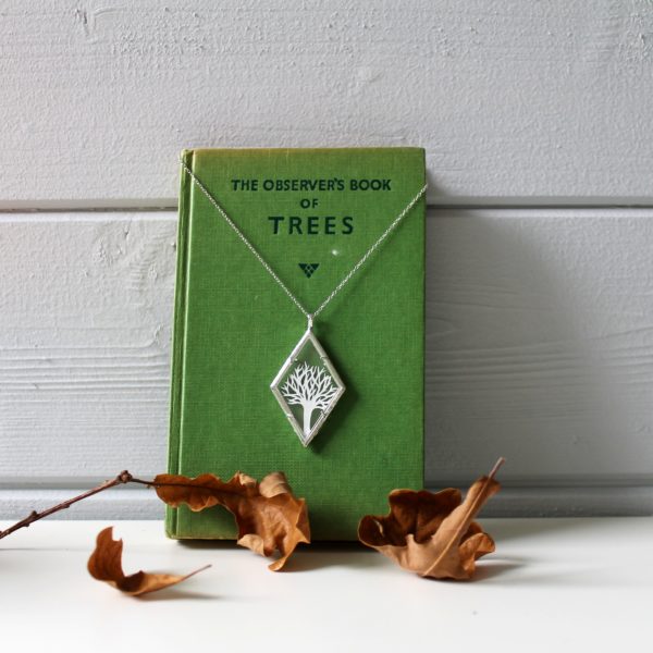 tree hand cut from white paper framed in a glass and plated silver diamond shaped necklace