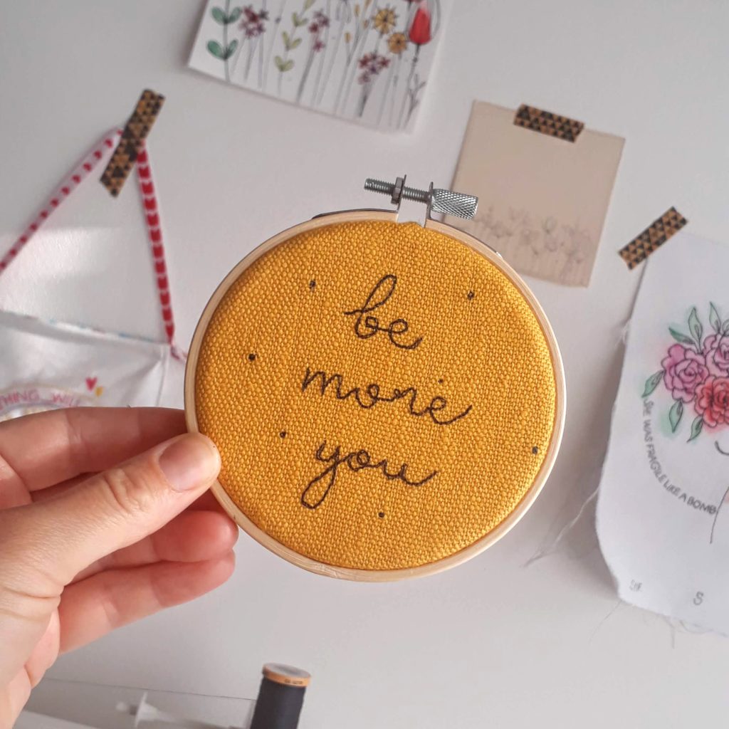 Be more you embroidered ono a mustard coloured linen and set in a 4" wooden embroidery hoop