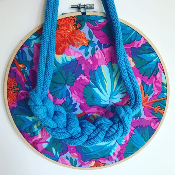 Loups, Bright blue rope necklace displayed in front of bright vintage fabric