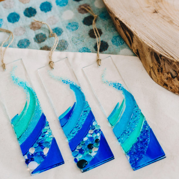 Glass at the Spinney, blue hanging wave made of fused glass in a variety of shades and glass beads, three are laying flat on display