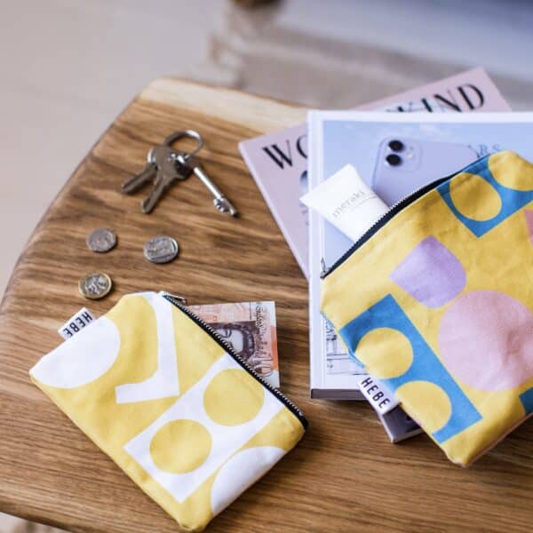 Yellow coin purse on a table with a medium sized pouch with phone and hand cream being put in.
