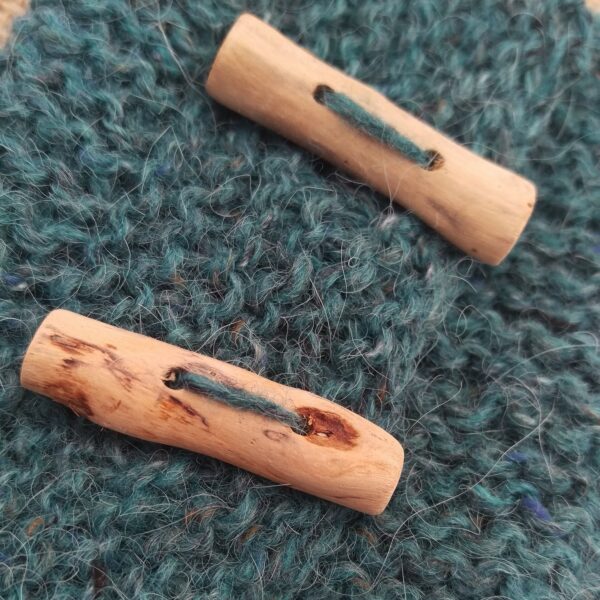 A close up of two pale driftwood buttons on soft turquoise knitting