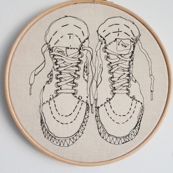Gemma Rappensberger Illustration of Vans Sk8-hi trainers using free motion machine embroidery in black thread with black hand embroidery details on calico, displayed in a 9" wooden embroidery hoop.