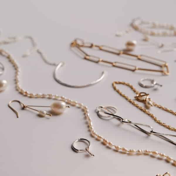 Flat lay of KiJo Jewellery crescent moon necklaces, pearls, earrings, and chain bracelets on light grey background