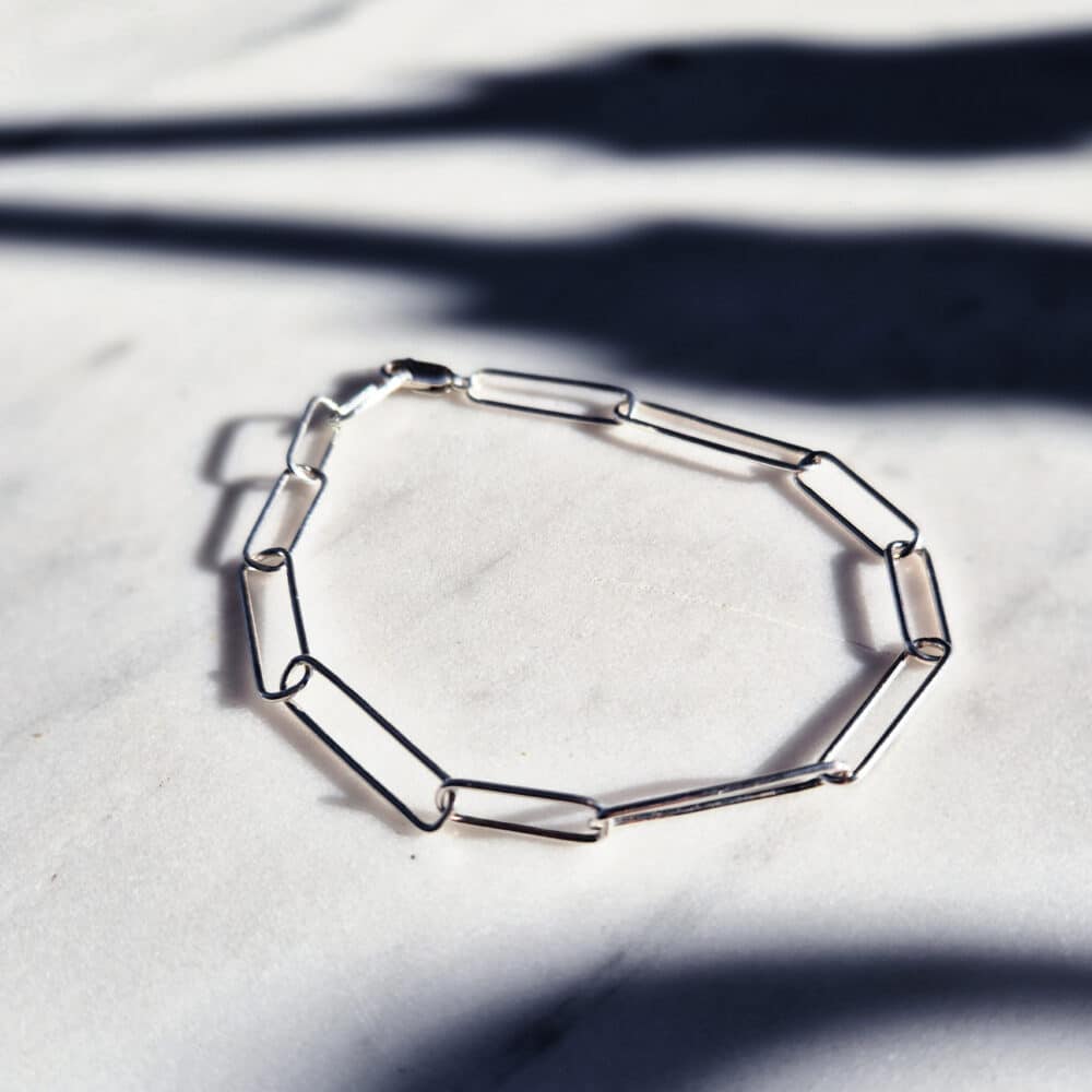 Handmade irregular paperclip silver chain bracelet displayed on a marble surface with strong blue shadows – minimal handmade jewellery flat lay.