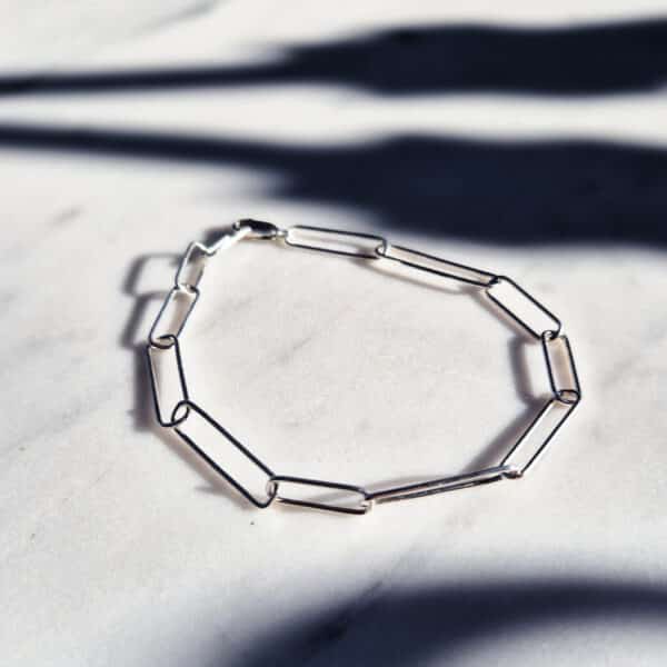 Handmade irregular paperclip silver chain bracelet displayed on a marble surface with strong blue shadows – minimal handmade jewellery flat lay.