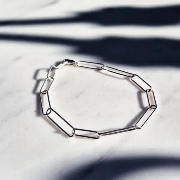 Handmade irregular paperclip silver chain bracelet displayed on a marble surface with strong blue shadows – minimal handmade jewellery flat lay.