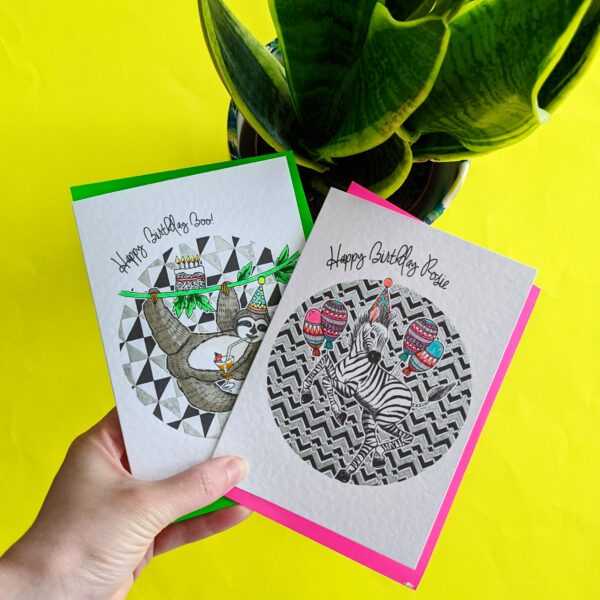 Katie Clement Illustration, Personalised Sloth and Zebra party animals Birthday cards with neon envelopes being held over a yellow background with a potted plant in the background.