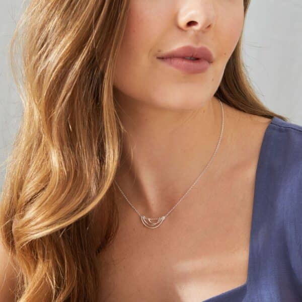 Modern silver interlocking necklace by KiJo Jewellery, styled on model in muted blue looking away from the camera