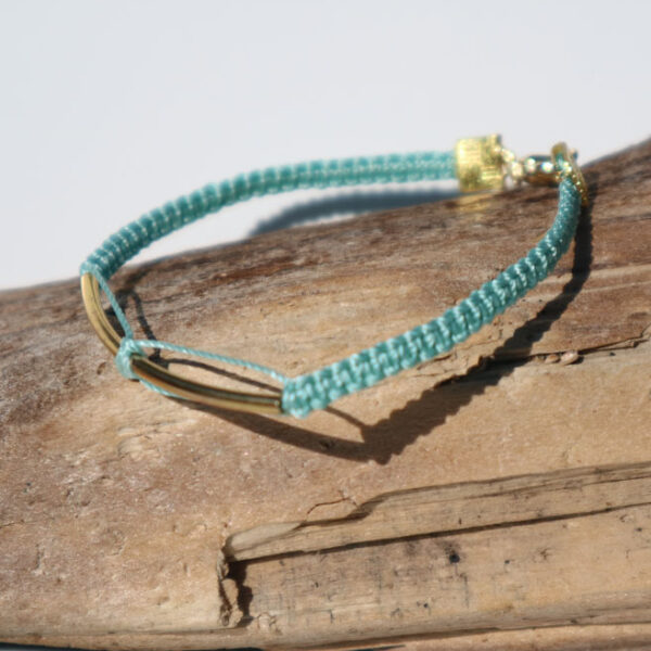 Gemma Thorpe macrame bracelet in teal yarn with gold coloured bar sat on driftwood