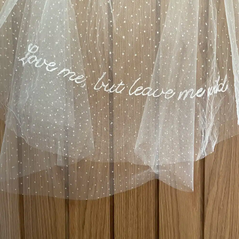 A wedding veil featuring delicate embroidered lettering with a personalised phrase stitched into the fabric.