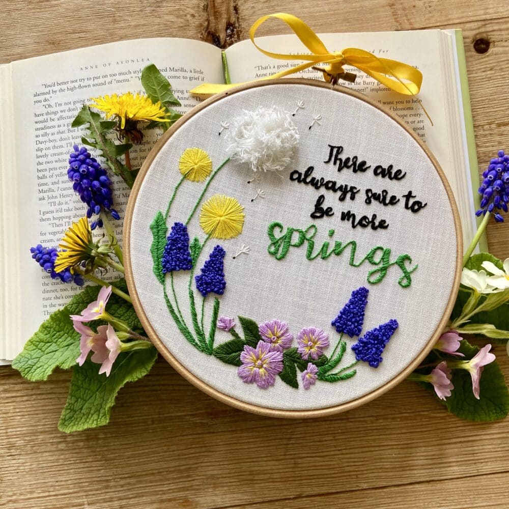 A floral embroidery kit inspired by Anne of Avonlea, featuring the quote “There Are Always Sure to Be More Springs” surrounded by embroidered dandelions, pansies, and muscari flowers.
