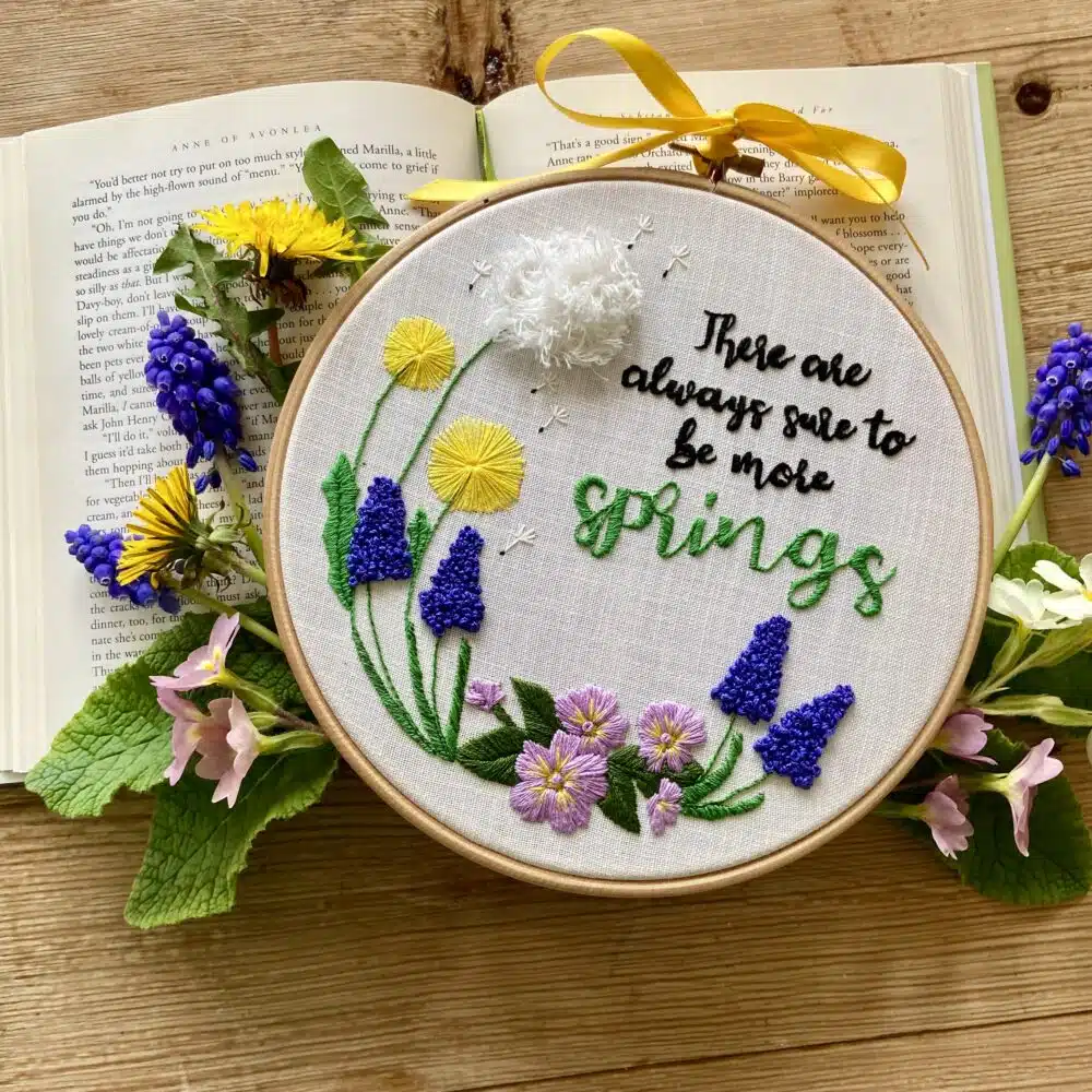 A floral embroidery kit inspired by Anne of Avonlea, featuring the quote “There Are Always Sure to Be More Springs” surrounded by embroidered dandelions, pansies, and muscari flowers.