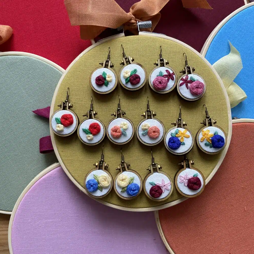 A pair of miniature embroidery hoop earrings featuring hand-embroidered floral designs, finished as wearable jewellery.
