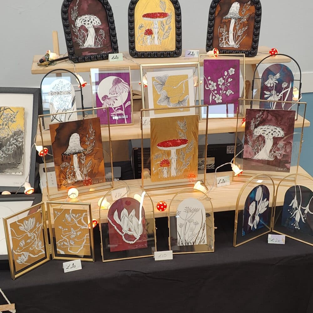 Art stall displaying framed artwork with a mix of mushrooms and flowers