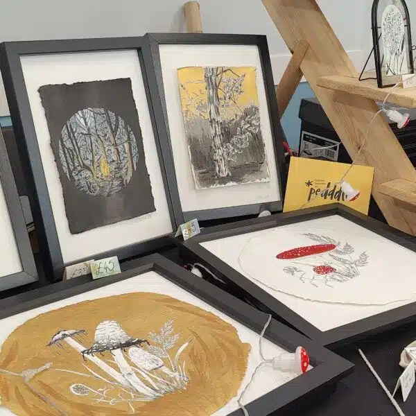 Art stall displaying framed artwork with a mix of different trees, mushrooms and flowers