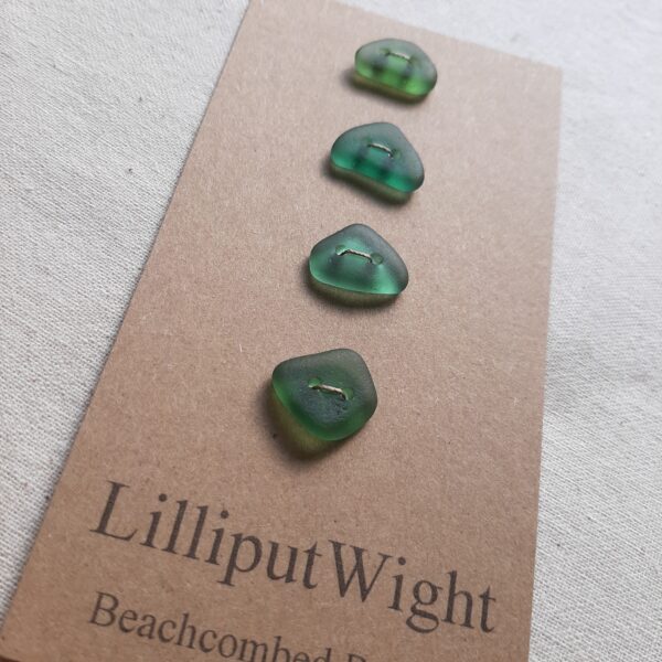 Four sea glass buttons in shades of blue green stitched to a brown card backing.