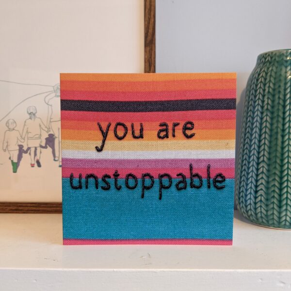 Little Light Stitchery Greetings card you are unstoppable. Square greetings card with a photo of a hand embroidered hoop stitched with the quote you are unstoppable on brightly coloured striped fabric