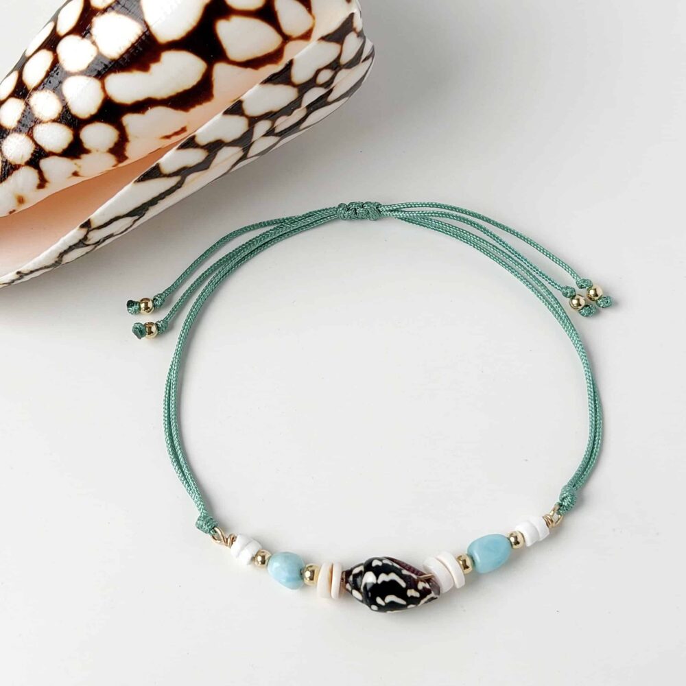 Hardy to Hudson teal cord bracelet with shell, Larimar and gold fill beads displayed on a white background next to a shell