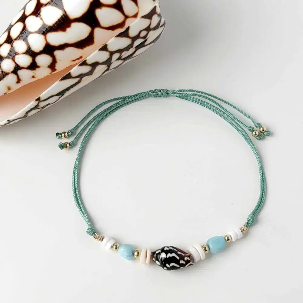 Hardy to Hudson teal cord bracelet with shell, Larimar and gold fill beads displayed on a white background next to a shell
