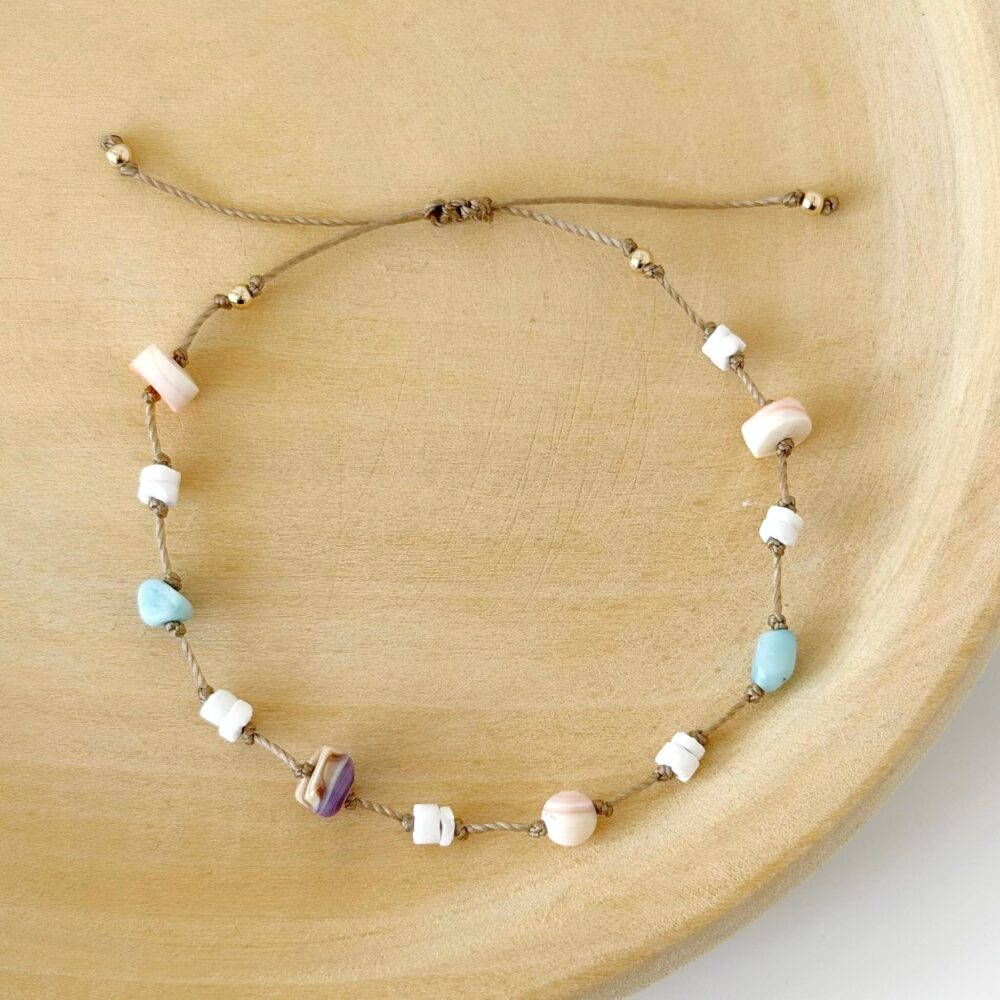 Hardy to Hudson beaded cord bracelet with shell beads on a beige nylon cord against a wooden background