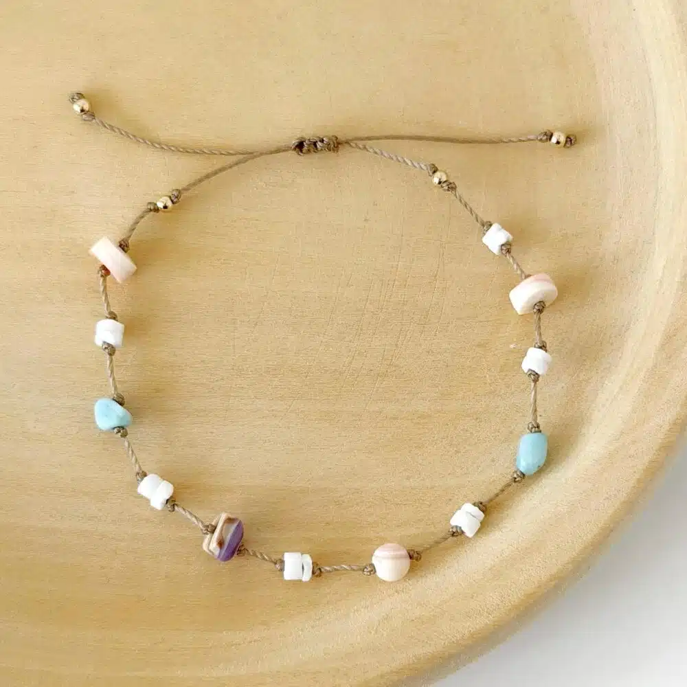 Hardy to Hudson beaded cord bracelet with shell beads on a beige nylon cord against a wooden background