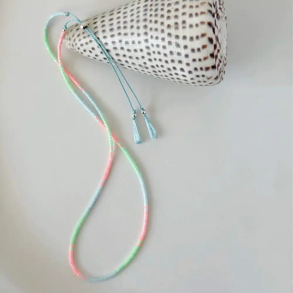 hardy to Hudson tiny delica bead double wrap silk beaded bracelet in pink, blue and green on a pale blue cord displayed next to a shell against white