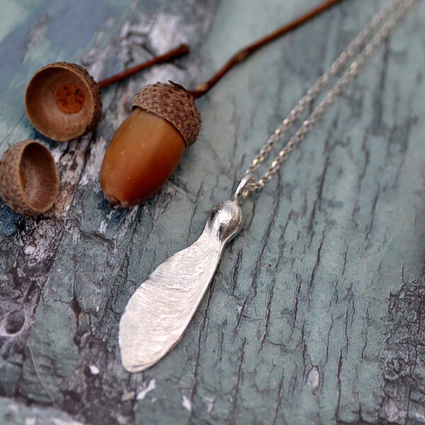 Upside Down Tree Studio, sycamore seed necklace on a rustic wooden board with acorns alongside