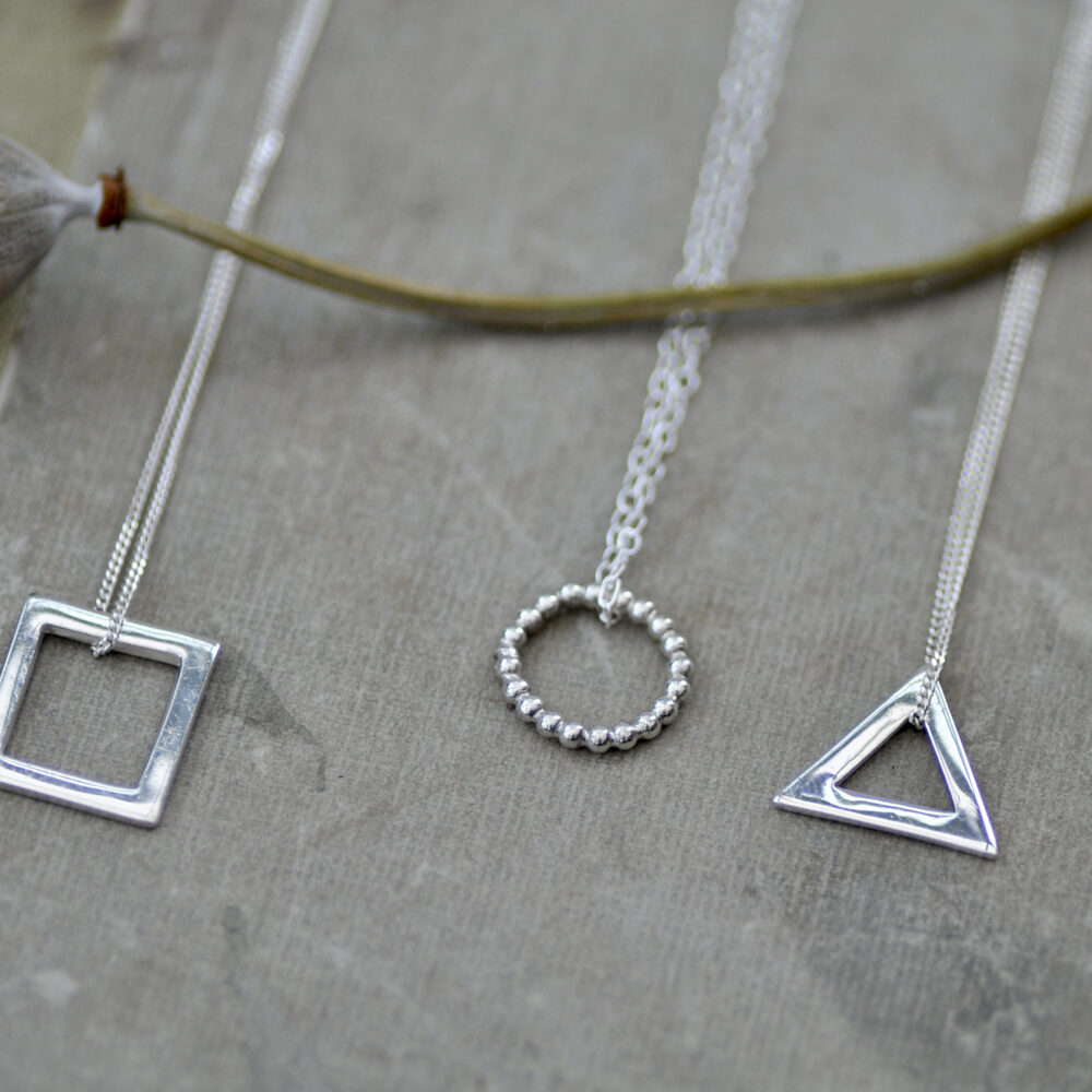 Upside Down Tree Studio, three geometric necklaces displayed on a vintage book with a poppy seed in the background