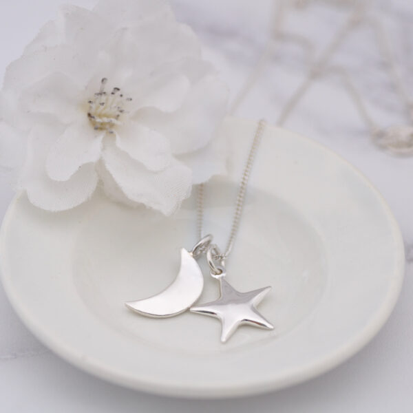 Upside Down Tree Studio, star and moon necklace displayed on a small vintage cream plate with a white flower