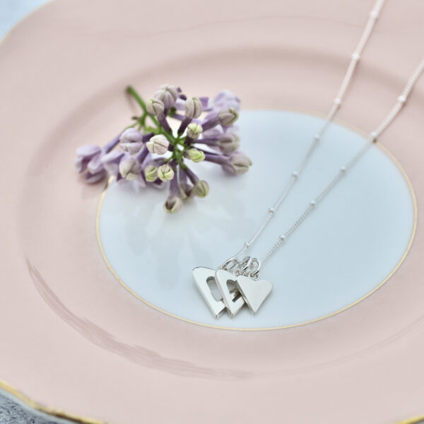 Upside Down Tree Studio, trio of hearts necklace on a vintage pink plate with lilac flower in the background