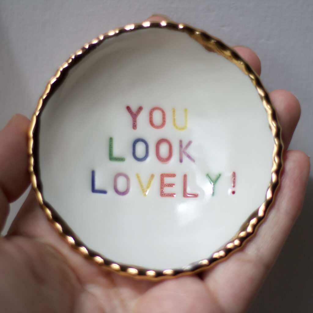Helen Manterfield a small ceramic bowl with gold scalloped edges and the message 'you look lovely' stamped and painted in a rainbow pattern