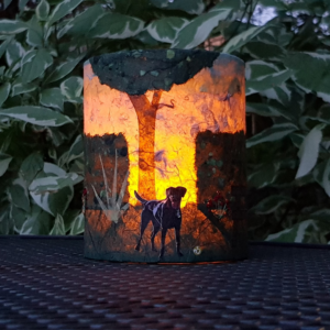 PeachTreePig - LED lantern with a collaged design with a black dog in a hedge-lined park. Shown with the candle lit up (© PeachTreePig)