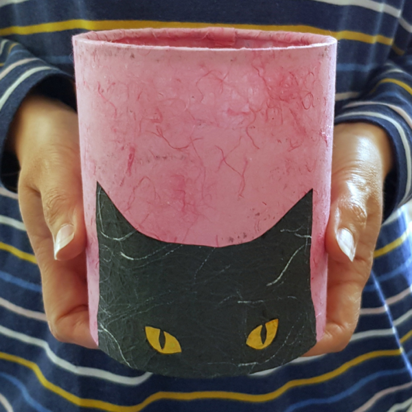 PeachTreePig - An LED lantern with a peeking black cat silhouette head on a pink background. Being held in hands (© PeachTreePig)