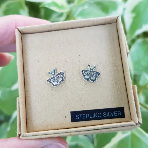 PeachTreePig - Sterling silver butterfly stud earrings, boxed and held against a background of leaves