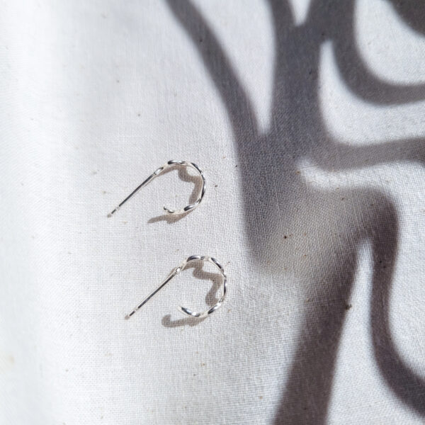 KiJo Jewellery, Wavy Silver Hoop Earrings taken from side view on natural fabric background and contrasting wavy shadows