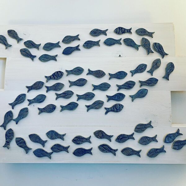 This is a ceramic fish picture called 'Shoal' ceramic fish on a whitewashed wooden board.