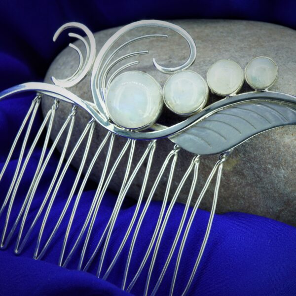 Art nouveau hair comb with 4 decending sized moonstones and swirl motifs resting again stone