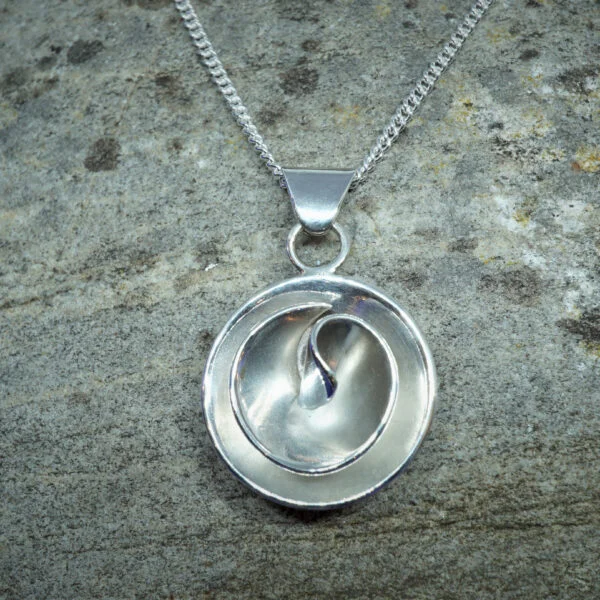 Contemporary circular sterling silver rose shaped pendant on chain with stone background.