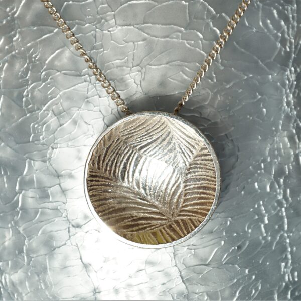 The Silver bird circular silver dome with leaf texture, hanging from chain with pale blue cracked glass background