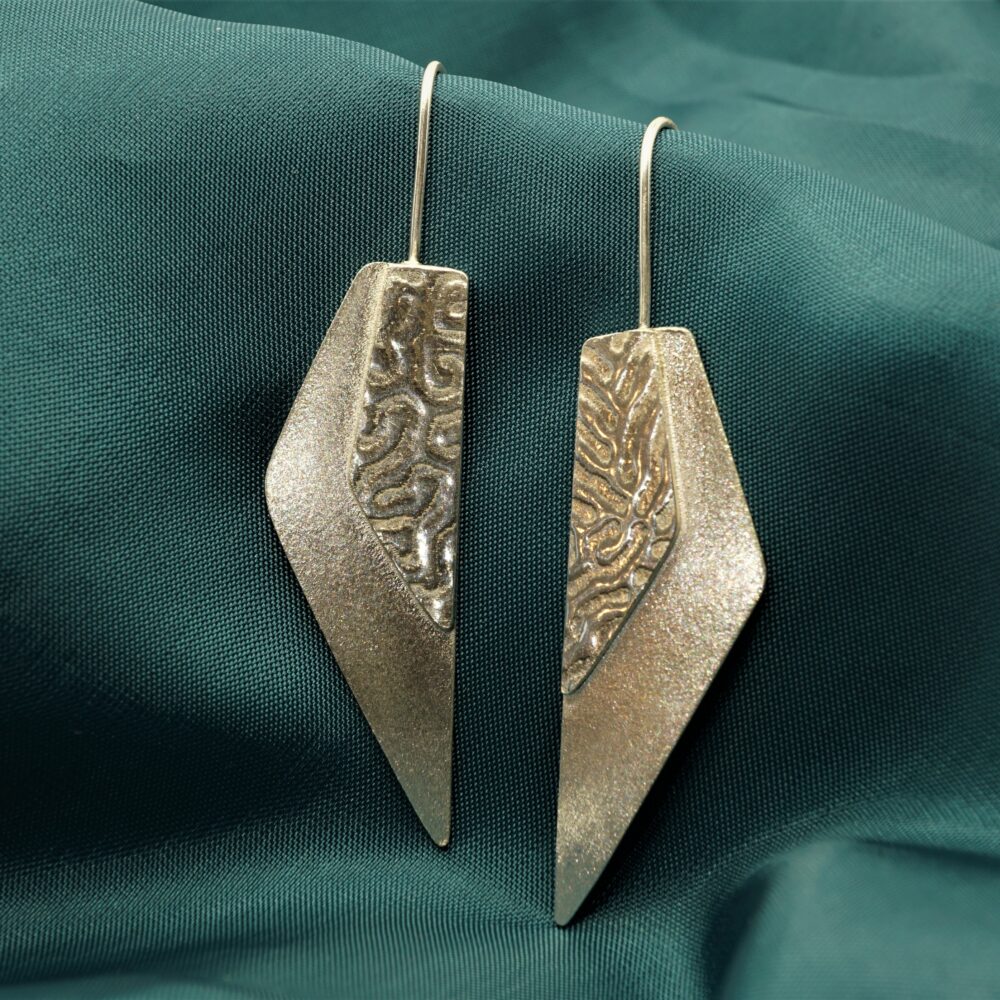 Handmade geometric triangular drop earrings with coral textured detail and contrasting frosted finish on silky turquoise background
