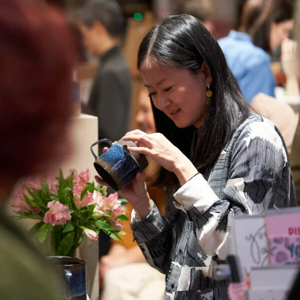 Shopper inspecting a handmade mug at Crafty Fox Market