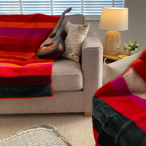 A view of two boldly striped deadstock sheepskin rug in reds, oranges and pinks, used as throws upon a sofa and armchair.