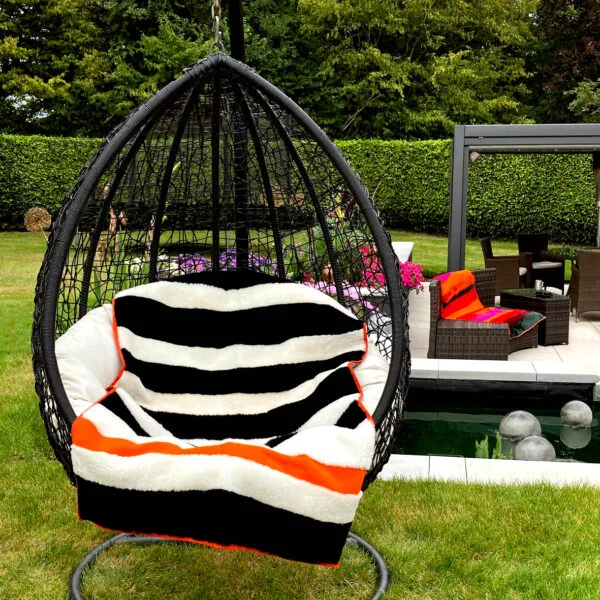 A view of two boldly striped deadstock sheepskin rug in black + white, used as a throw on a garden swing chair.