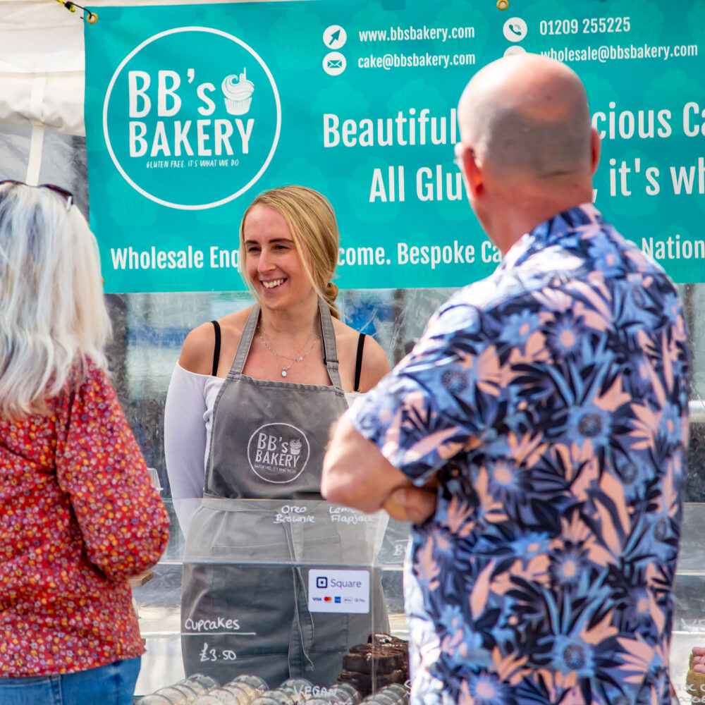 Customers chatting to a market stall trader who sells baked goods and cakes