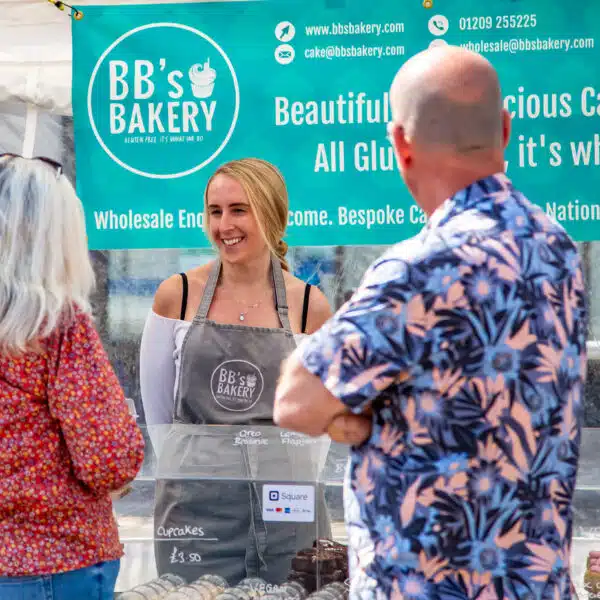 Customers chatting to a market stall trader who sells baked goods and cakes