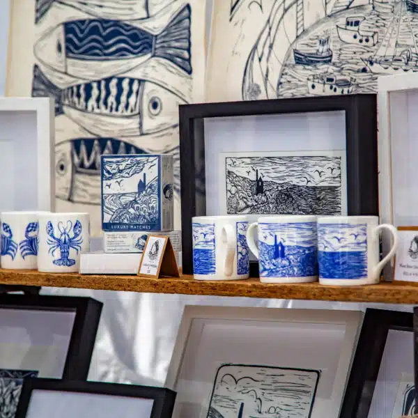 Market stall stands with a display of blue and white lino printed prints, mugs and tea towels